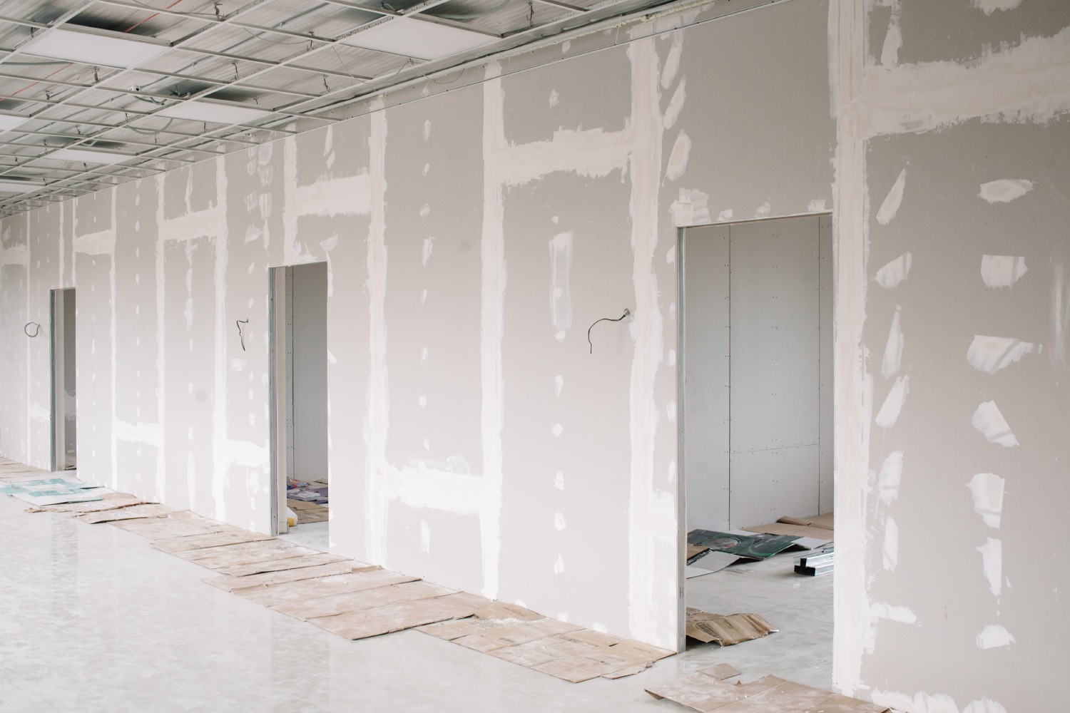 A partially finished interior with drywall and unfinished doorways, surrounded by construction debris and floor protection on polished concrete.