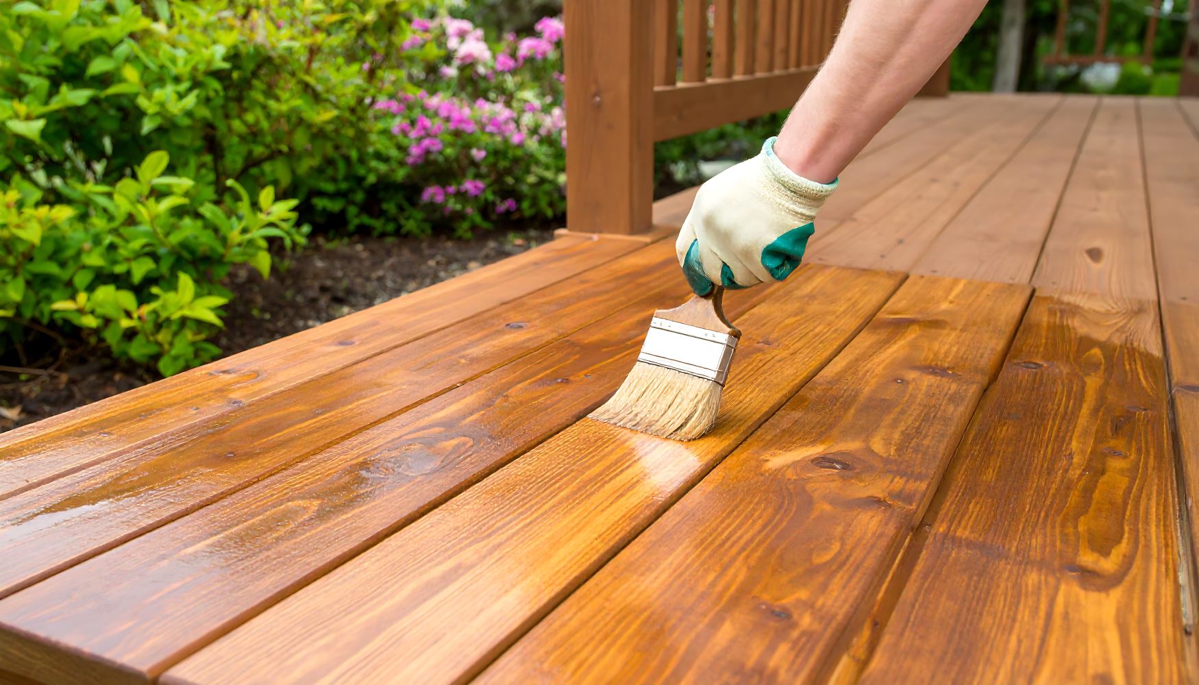 Person applying wood stain or varnish to an outdoor wooden deck using a brush, enhancing and protecting the wood’s natural finish.