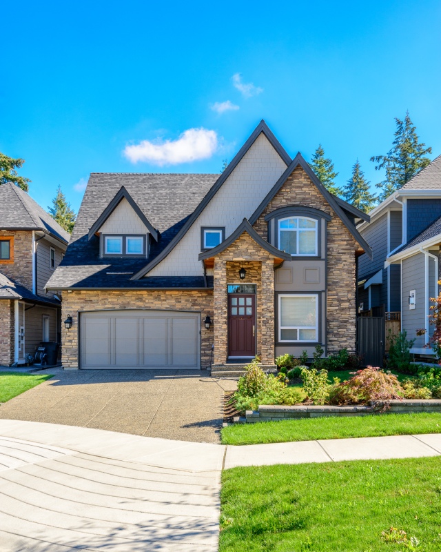 A modern two-story home with stone accents, a brown door, and a well-kept garden, set against a clear blue sky.