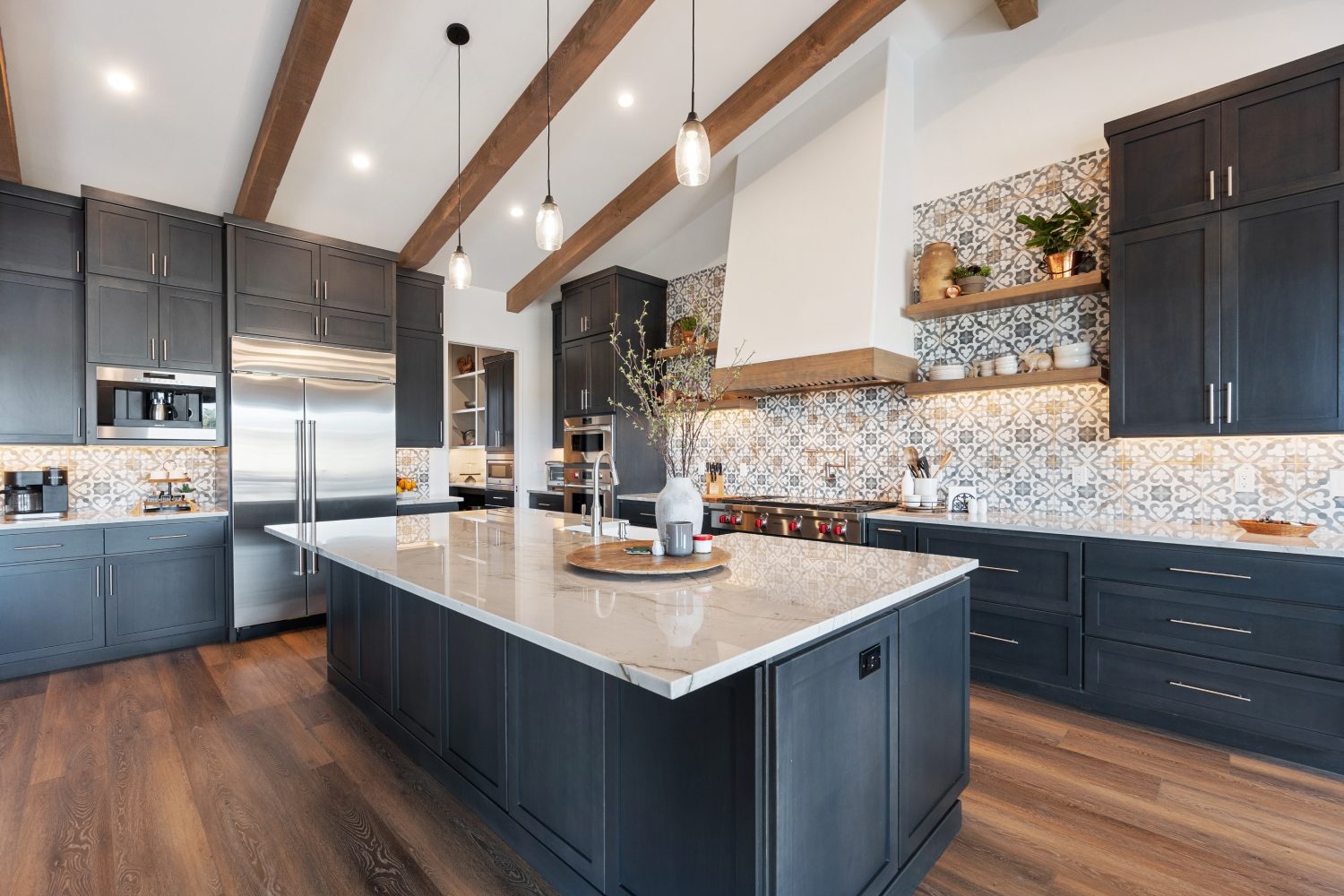 Sleek kitchen with dark cabinets, light marble island, and wooden beams. Patterned backsplash and pendant lights create a modern yet cozy vibe.